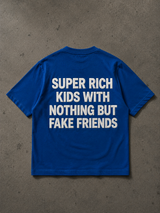 A royal blue short-sleeve t-shirt with bold white text reading 'SUPER RICH KIDS WITH NOTHING BUT FAKE FRIENDS' printed on the back, laid flat on a textured gray concrete surface.