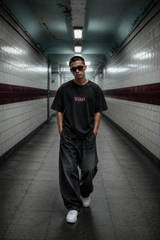 Person wearing sunglasses and a black t-shirt in a tiled hallway
